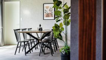 A dining area with a round table and chairs, a potted plant, and a framed artwork on the wall.