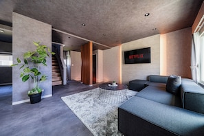 Un salon moderne avec un canapé gris, une table basse et un grand téléviseur à écran plat fixé au mur.
