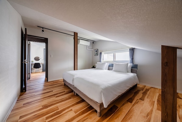 Une chambre à coucher avec un grand lit, un plancher en bois, une fenêtre avec des rideaux et un appareil de climatisation fixé au plafond.