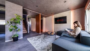 A modern living room with a sofa, a coffee table, and a large TV screen displaying the Netflix logo.
