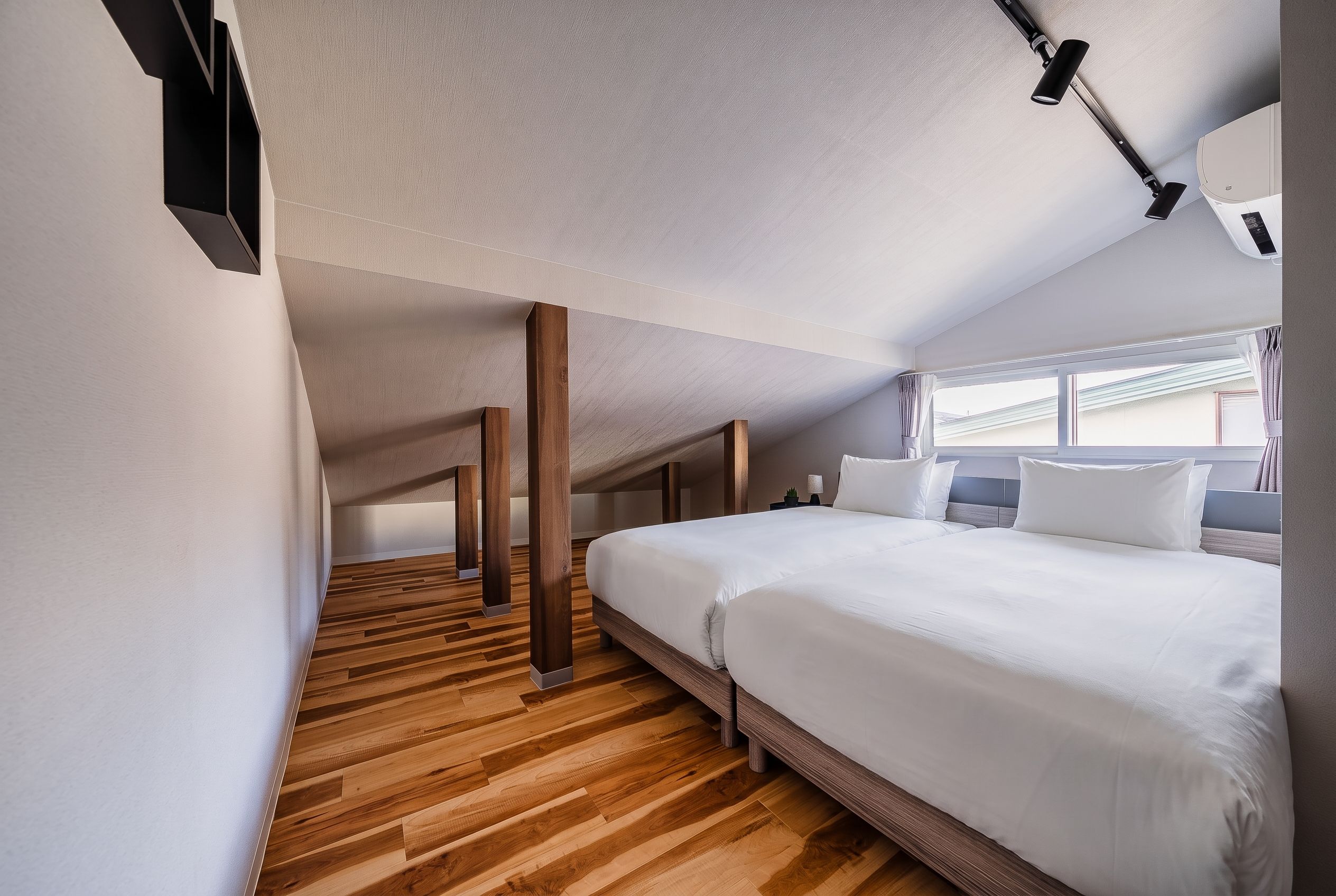 Una habitación de hotel moderna con una cama grande, suelo de madera y una lámpara fijada al techo.