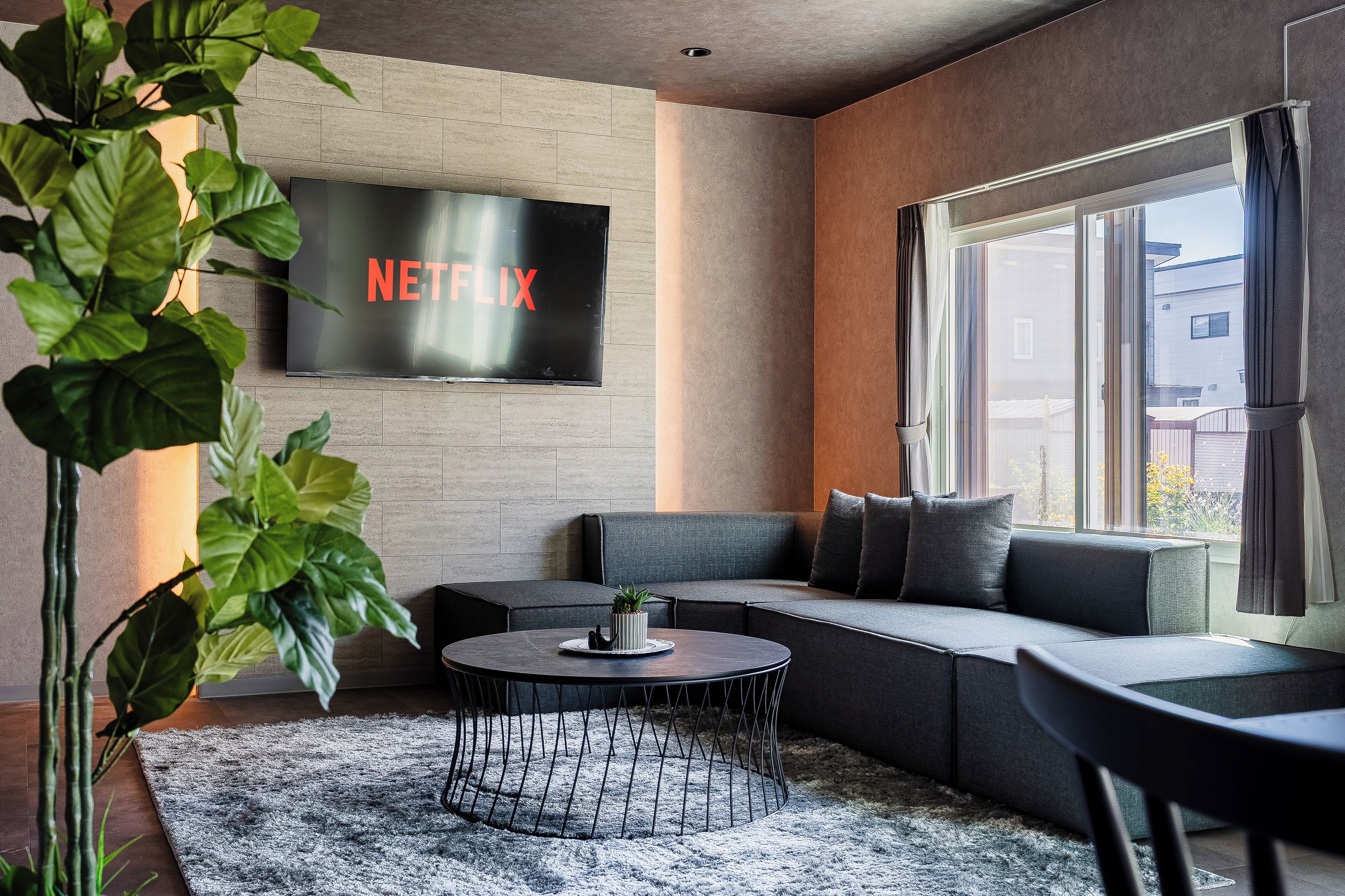 Una sala de estar moderna con un sofá modular, una mesa redonda de centro y un televisor de pantalla plana grande montado en la pared.