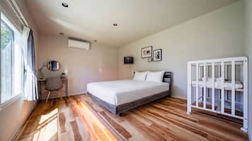 A bedroom with a bed, a crib, a desk with a chair, and a window.