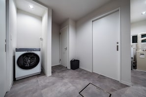 Une buanderie équipée d’un lave-linge à chargement frontal, d’une poubelle et d’une porte donnant sur une autre pièce.