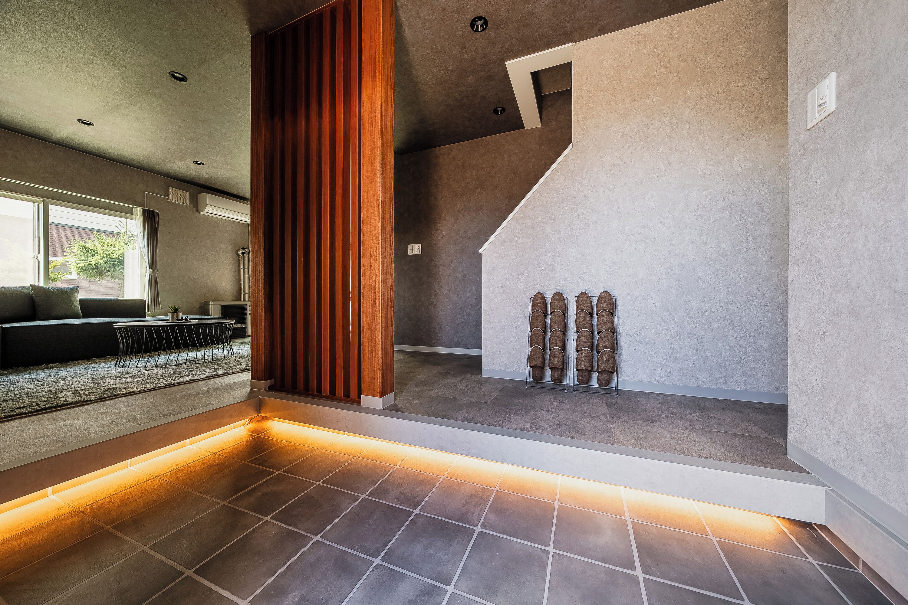 A modern interior with a staircase, a seating area with a sofa and table, and a shoe rack.