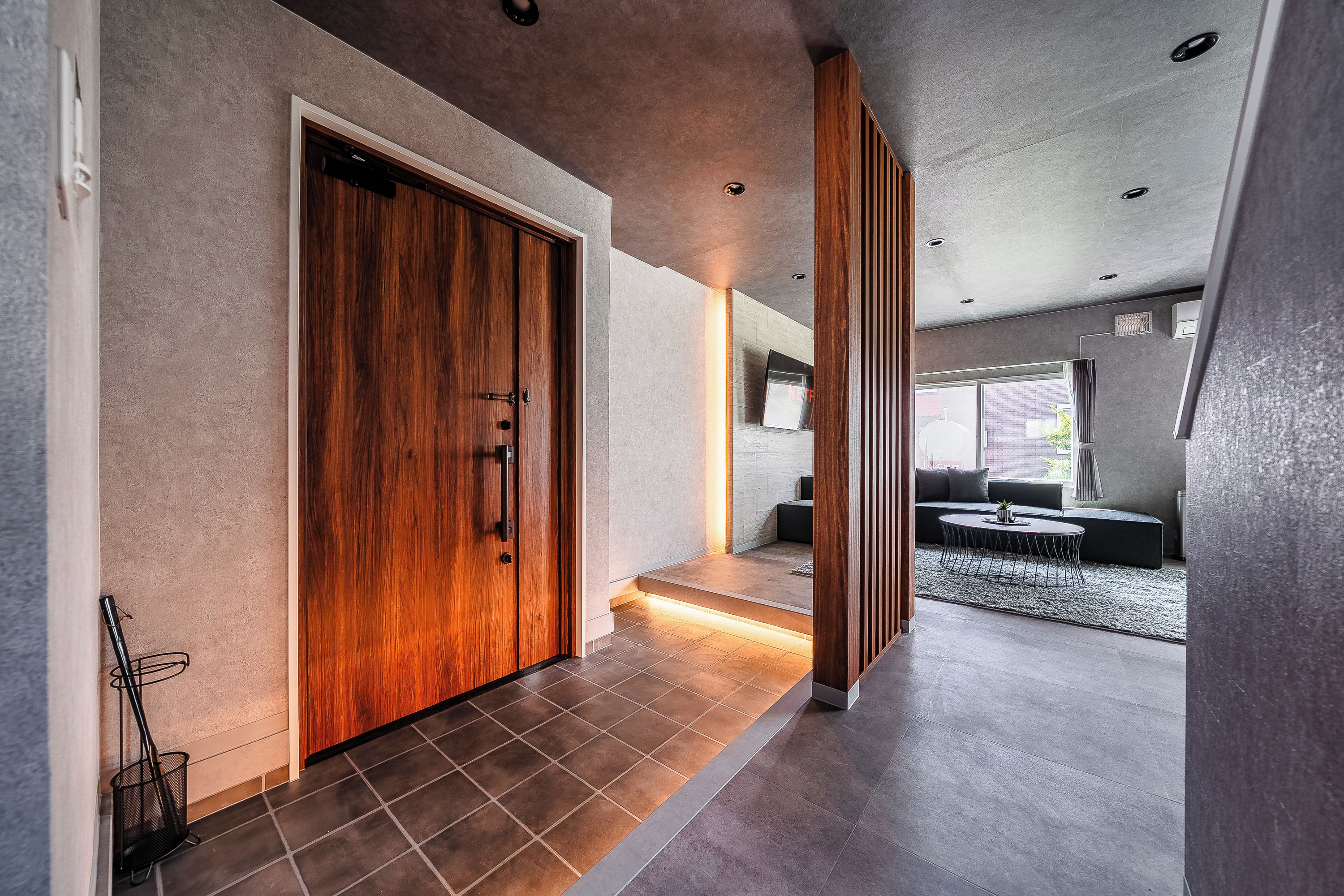 A modern hallway with a wooden door, a staircase, and a seating area with a sofa and coffee table.