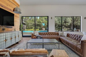 A modern living room with a sectional sofa, a coffee table, and a TV mounted on a wooden wall. - Modern Oasis w Pool, Hot tub, Outdoors, Close to Austin and Dripping Springs (Austin)