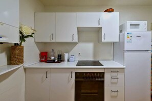 Eine kleine Küche mit weißen Schränken, einer Mikrowelle, einem Backofen und einer Kaffeemaschine.