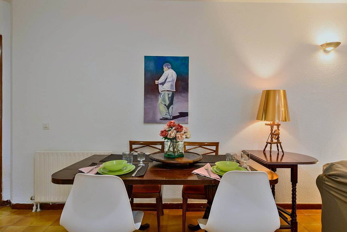 Un'area pranzo con un tavolo apparecchiato per due, un vaso di fiori e un quadro appeso al muro.