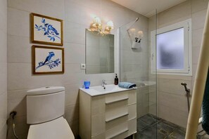 Un baño con inodoro, lavamanos con espejo y zona de ducha.