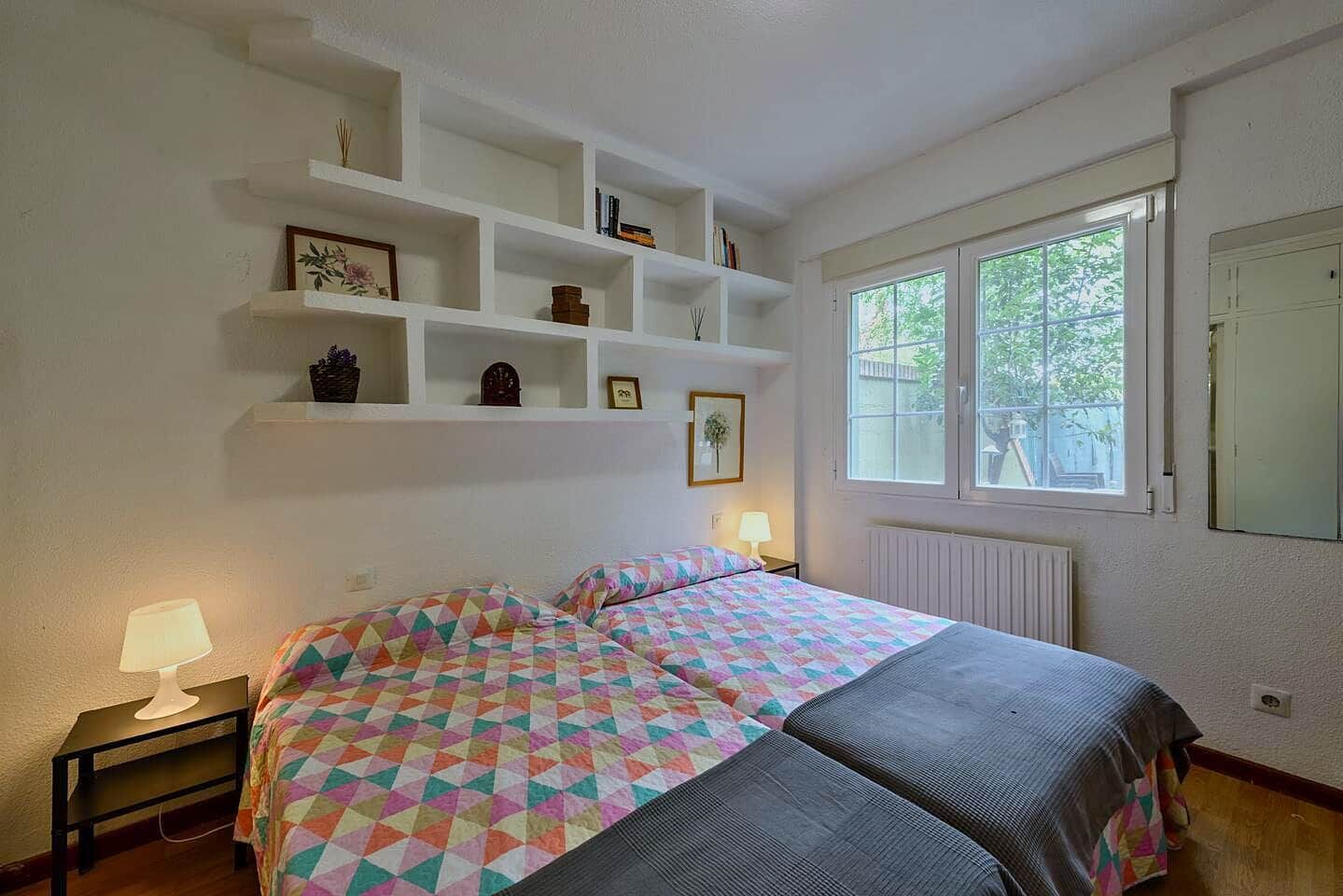 Ein Schlafzimmer mit einem Bett, Nachttischlampen, einem Fenster und eingebauten Regalen mit verschiedenen Gegenständen.