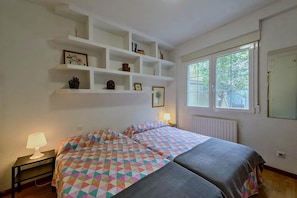 Ein Schlafzimmer mit einem Bett, Nachttischlampen, einem Fenster und eingebauten Regalen mit verschiedenen Gegenständen.