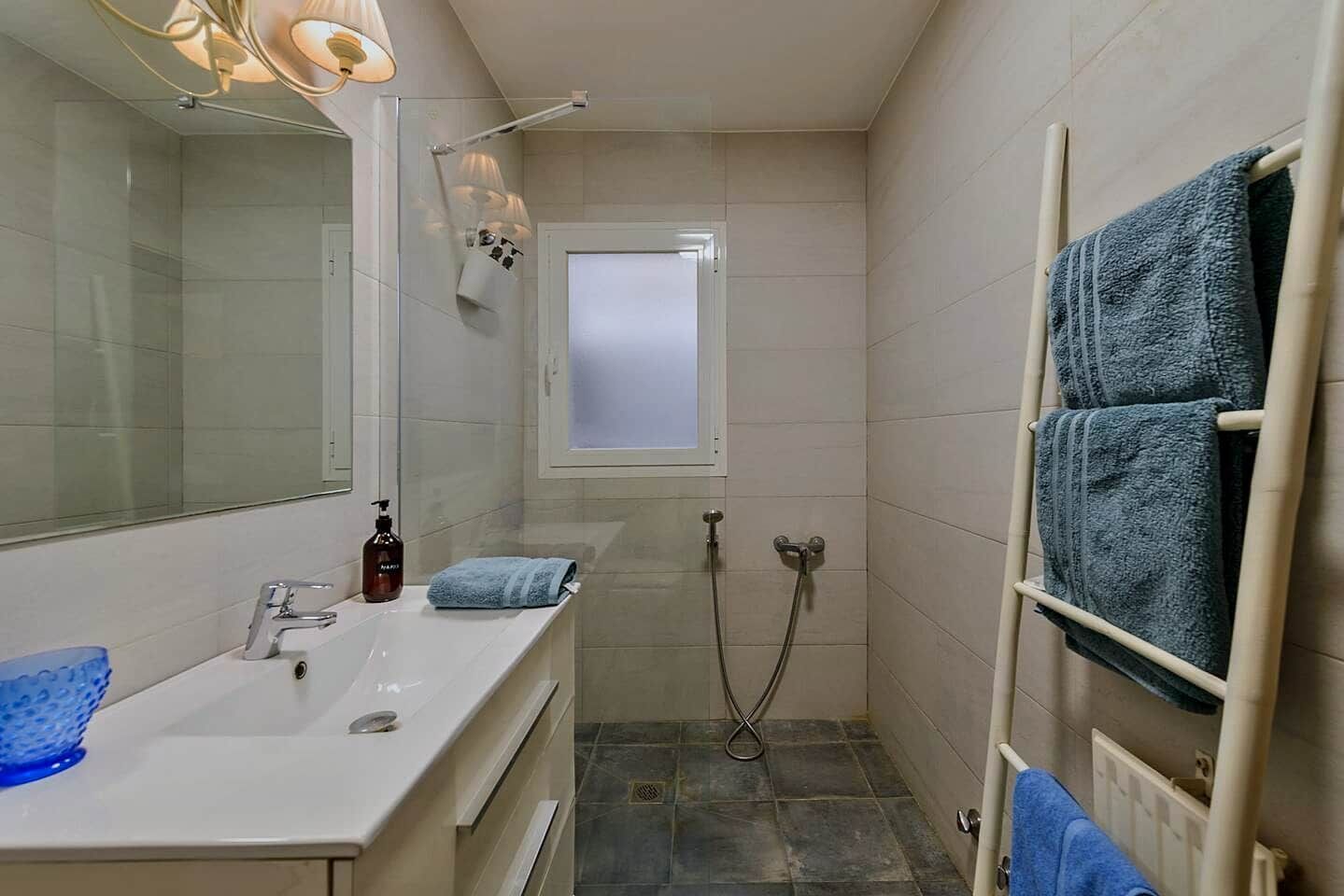 Een badkamer met een wit wastafel, een spiegel, een douche en een handdoekrek.