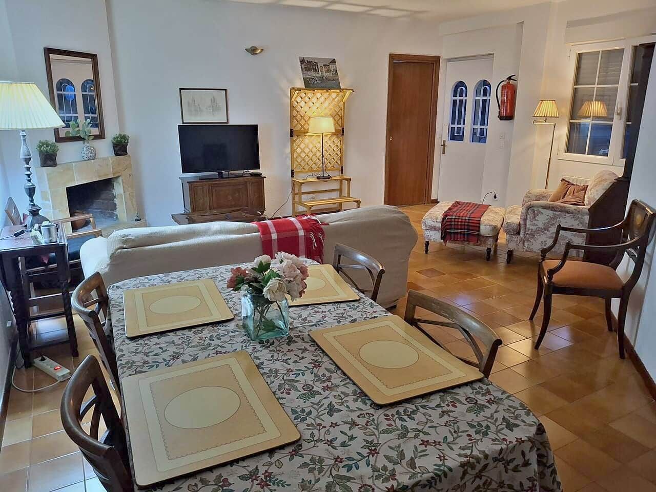 Un salon chaleureux avec une cheminée, un téléviseur et un coin repas agrémenté de sets de table et d’un vase de fleurs.