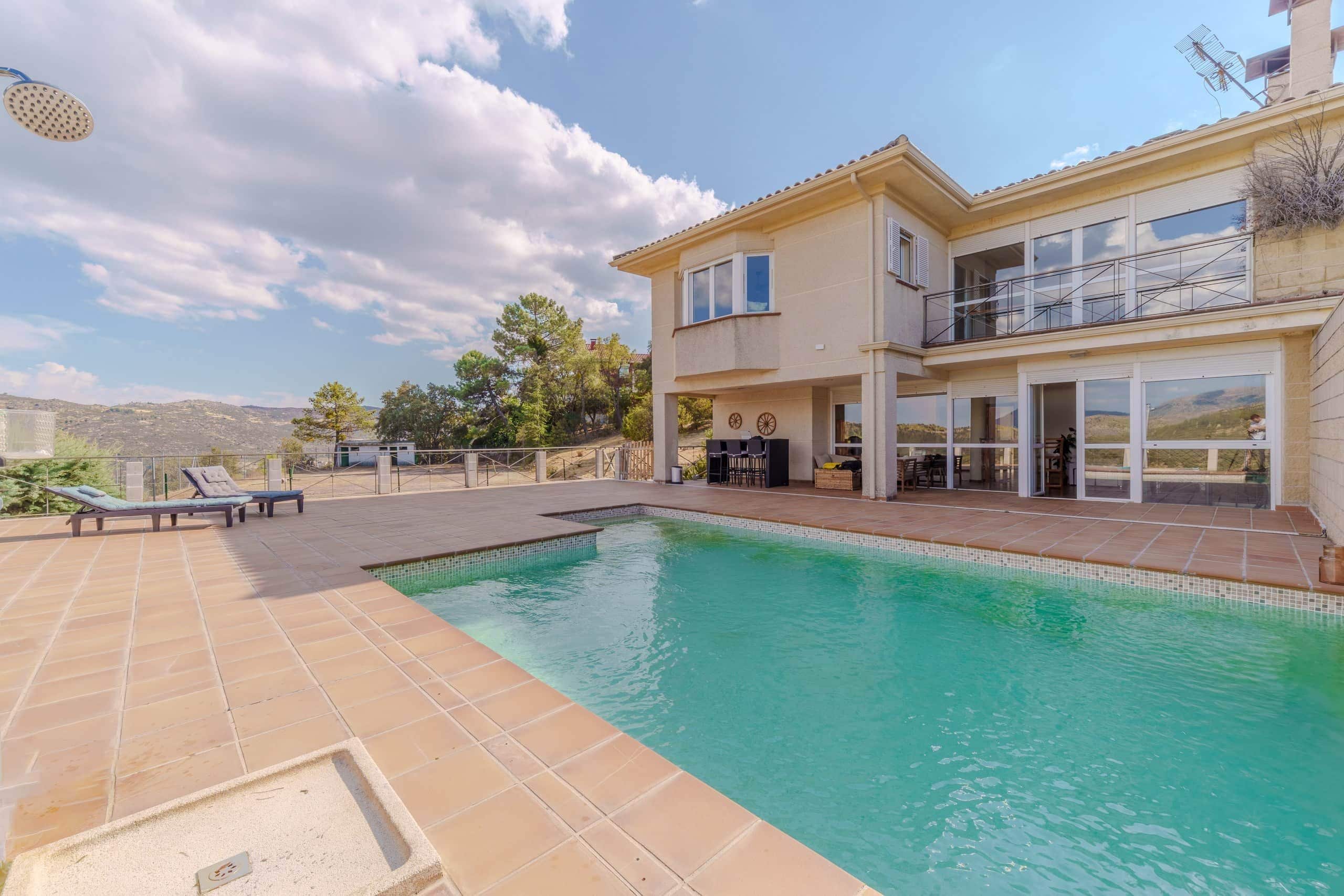 A two-story building with a swimming pool, outdoor seating, and a view of the surrounding landscape.