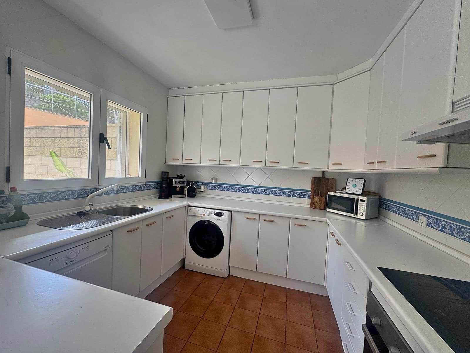 Une cuisine compacte avec des meubles blancs, un lave-linge, un four à micro-ondes et un évier.