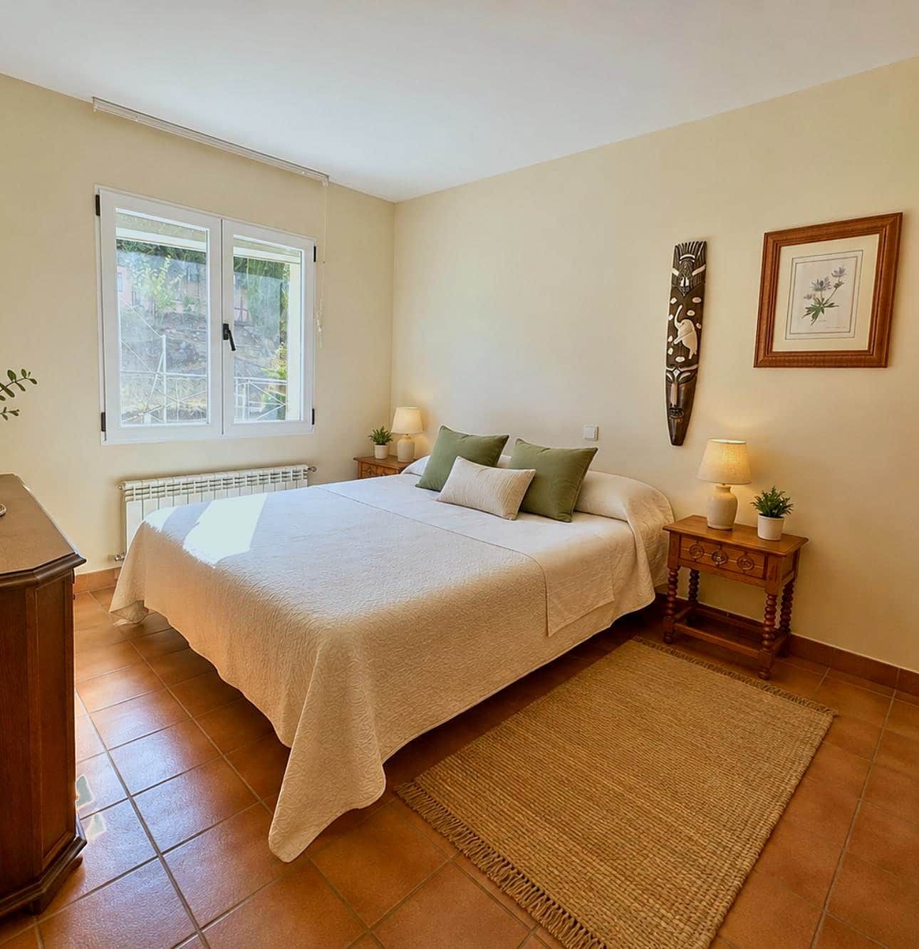 Une chambre à coucher comprenant un lit, une fenêtre, un radiateur, une table de chevet avec une lampe et une œuvre d’art accrochée au mur.