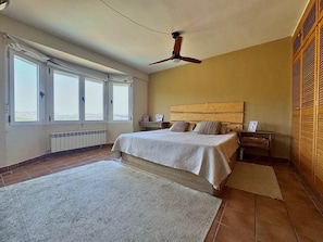 Een slaapkamer met een bed, een nachtkastje, een plafondventilator en uitzicht door grote ramen.