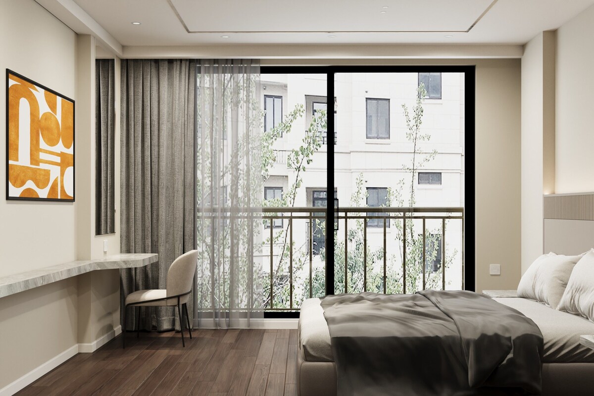A modern bedroom with a large bed, a chair, a desk, and a balcony with a view of buildings.