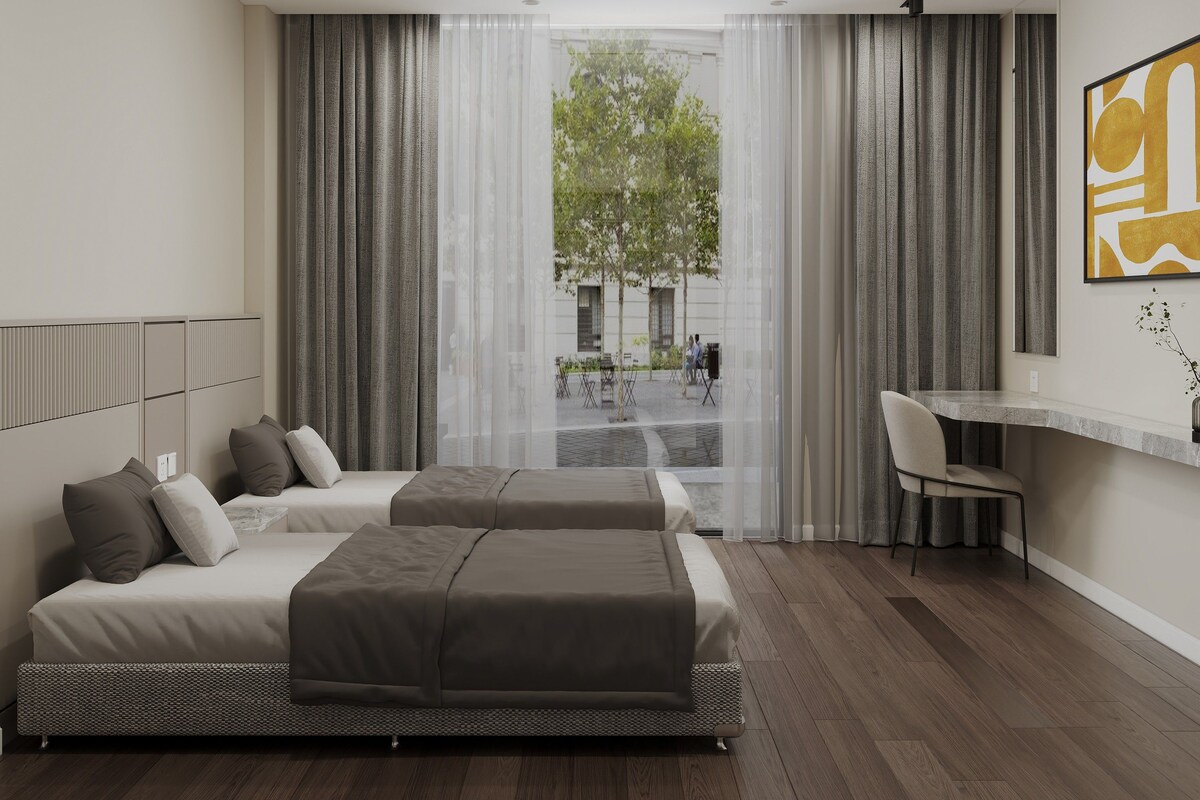A modern hotel room with a bed, a desk, and a view of the outside.