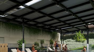 Una piscina interior con sillones de descanso, una zona techada y vistas al exterior.