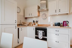 A kitchen with white cabinets, a stainless steel range hood, a dishwasher, and a red kettle. - Hoglets - Cosy Countryside Retreat (Conderton)