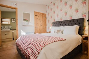 A bedroom with a large bed, a wooden wardrobe, a mirror, and a floral wallpaper. - Hoglets - Cosy Countryside Retreat (Conderton)