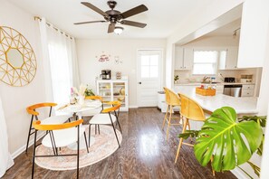 A modern kitchen with white cabinets, a dining area with yellow chairs, and a ceiling fan. - Furnished 4BR Home Workspace & Extended Stays (Silver Spring)