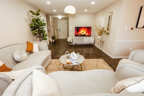 A modern living room with a fireplace, sofas, a coffee table, and a television. - Furnished 4BR Home Workspace & Extended Stays (Silver Spring)