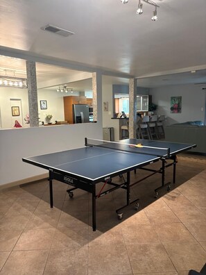 A ping pong table in a room with a tiled floor, a kitchen area in the background, and a dining area with chairs. - Maison Grape  Elegant 3BR Home near Medical Center & NRG (Houston)