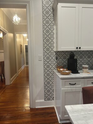 Cocina con armarios blancos, encimera de mármol y salpicadero estampado.