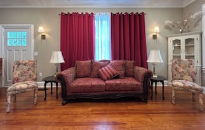 Una sala de estar con un sofá, dos sillones, un aparador y una ventana con cortinas.