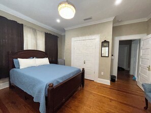 Un dormitorio con una cama de madera, una puerta blanca y un pasillo que conduce a otra habitación.