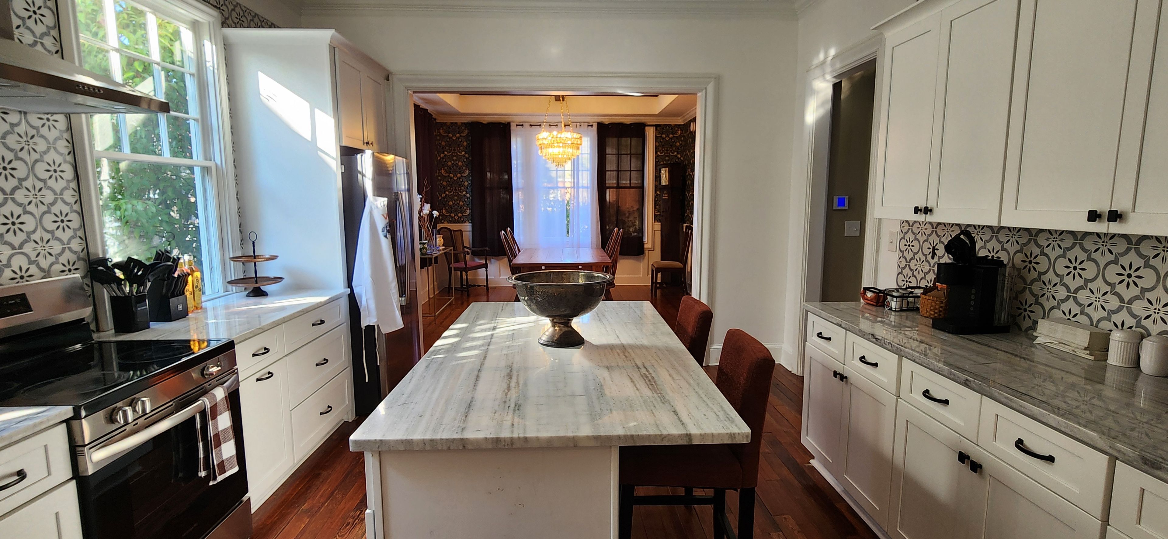 A kitchen with white cabinets, a marble countertop, and a large island with a bowl.