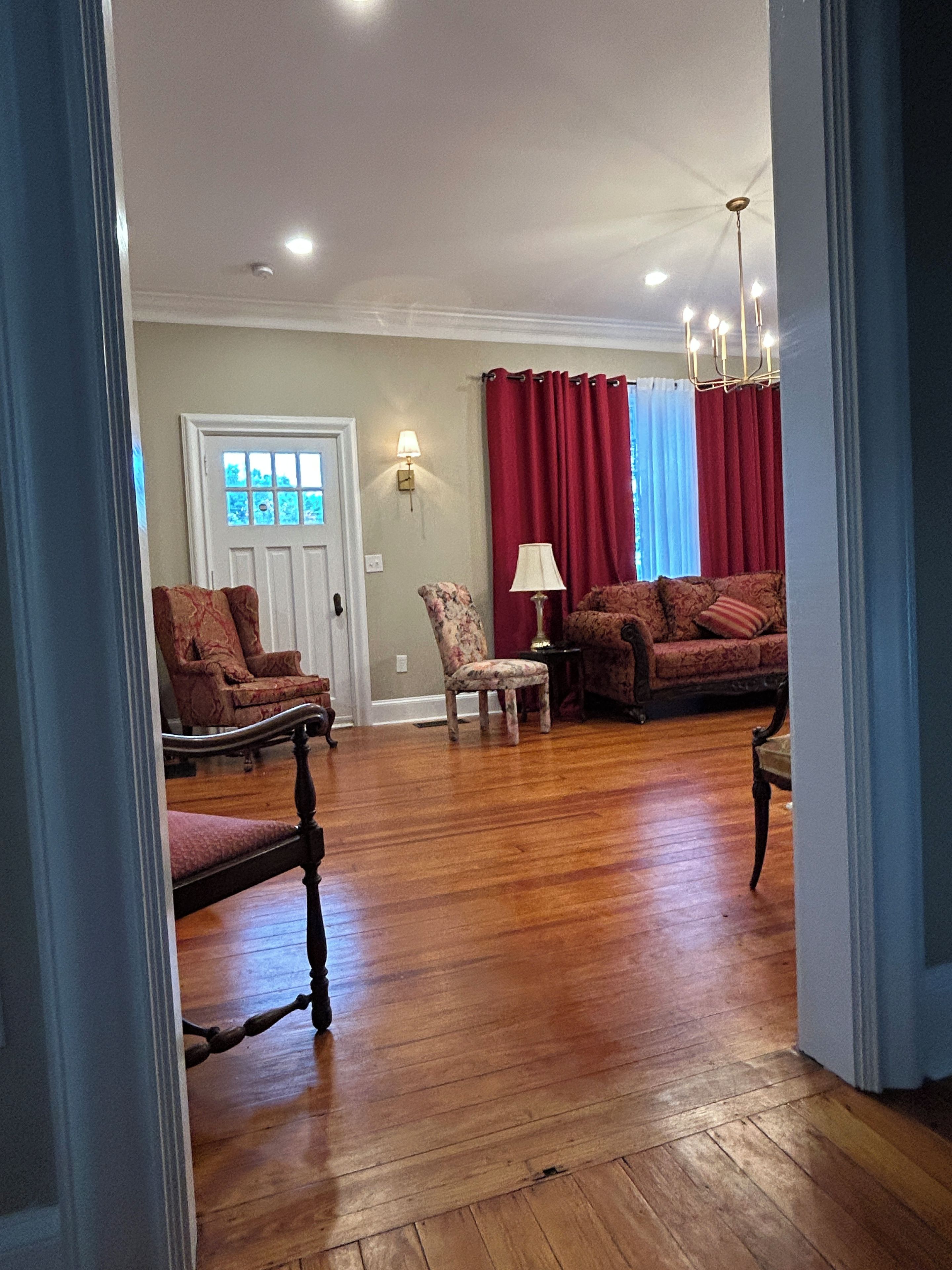 A living room with hardwood flooring, a door, a red curtain, and two lamps.