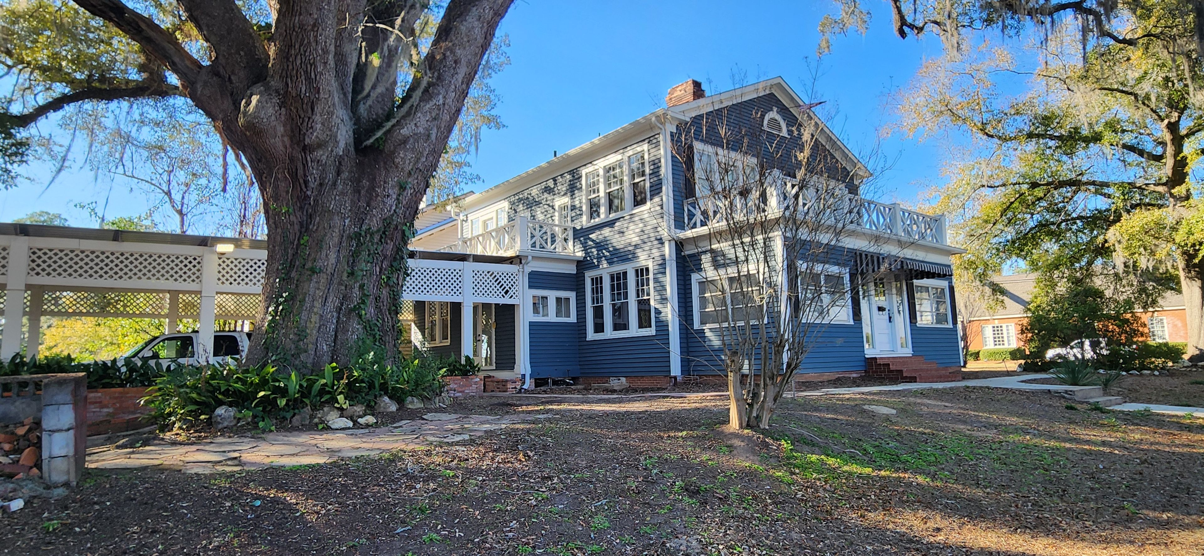 A two-story house with a large tree in front, a covered porch, and a brick pathway leading to the entrance.