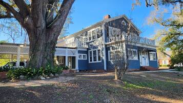 A two-story house with a large tree in front, a covered porch, and a brick pathway leading to the entrance.