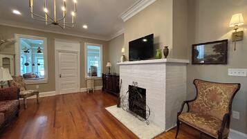 A living room with hardwood flooring, a white fireplace, a television on the mantel, and a chandelier.