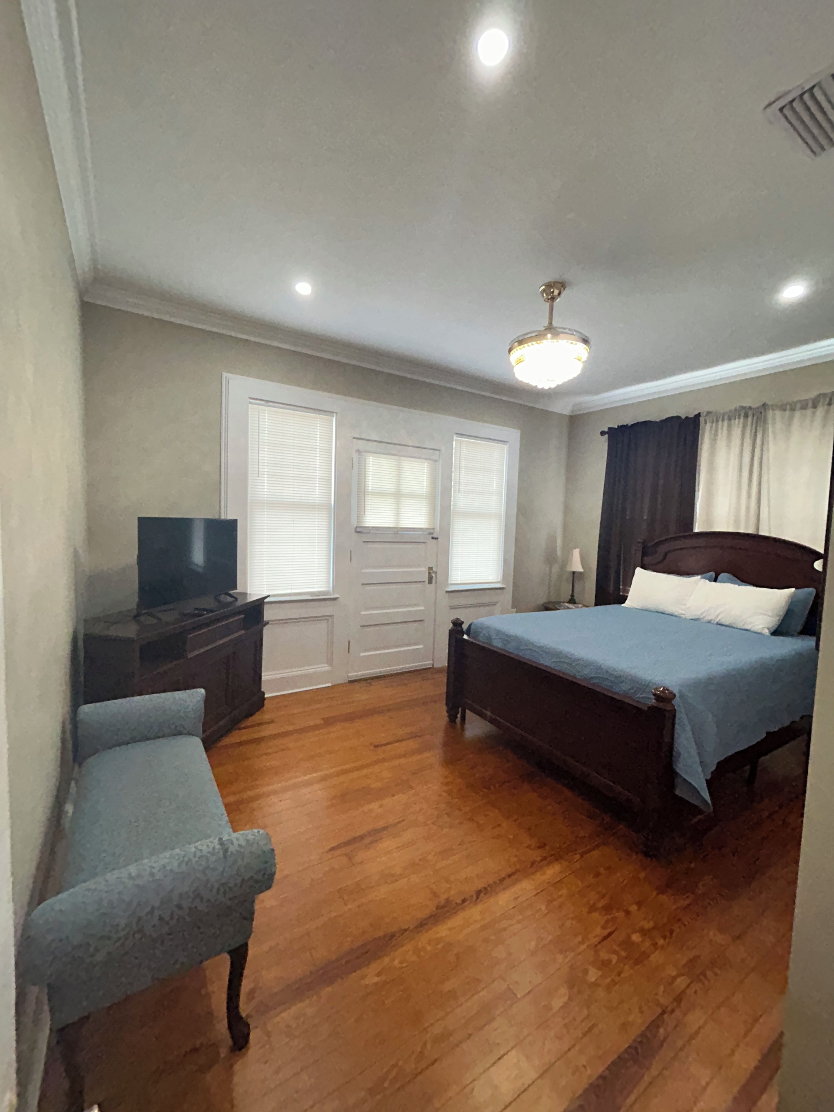 A bedroom with a bed, a TV, a bench, and a ceiling light.