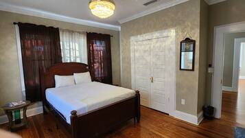 A bedroom with a wooden bed, a nightstand, a dresser, a chandelier, and a door with a mirror.