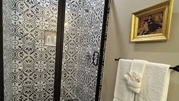 A shower with a patterned tile design, a gold-framed picture on the wall, and a towel rack with towels.