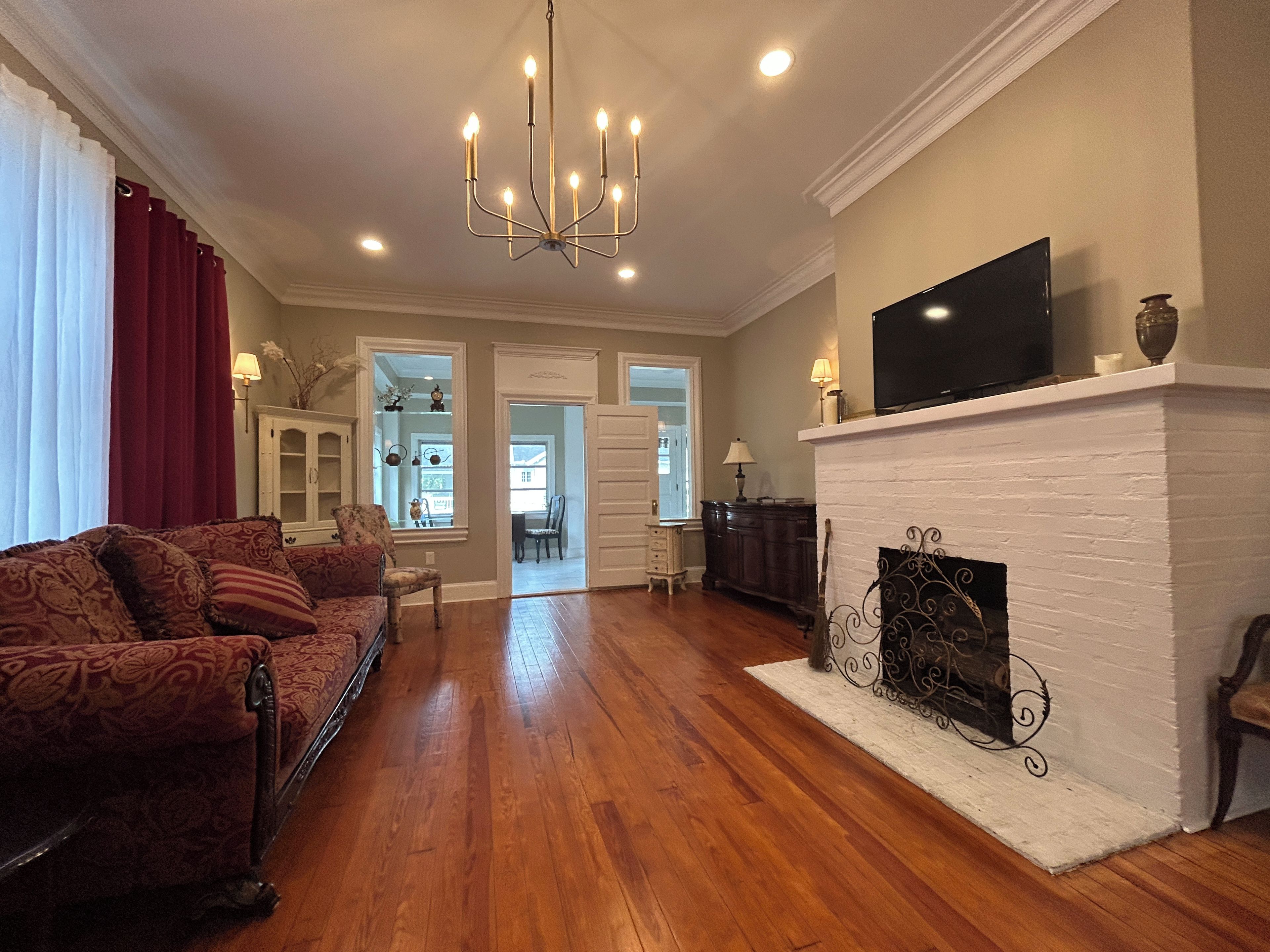 A living room with a fireplace, a television mounted above it, and a chandelier.