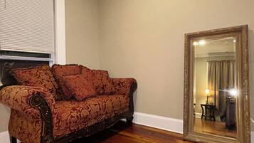 Una habitación con un sofá estampado, un espejo grande y una ventana con persianas.
