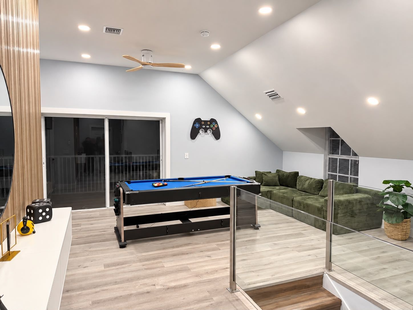 A modern living room with a pool table, a ceiling fan, and a gaming console on the wall.