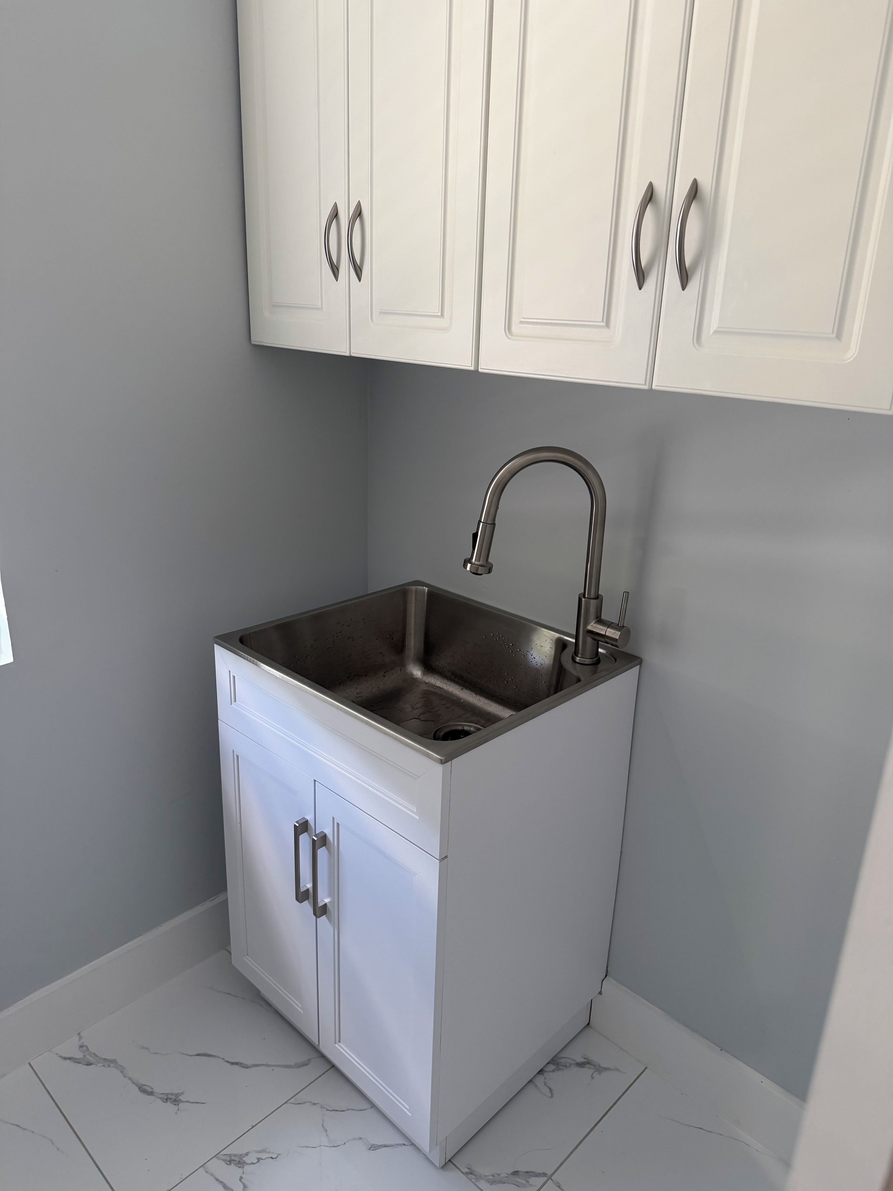 A compact kitchen with white cabinets, a stainless steel sink, and a marble-tiled floor.