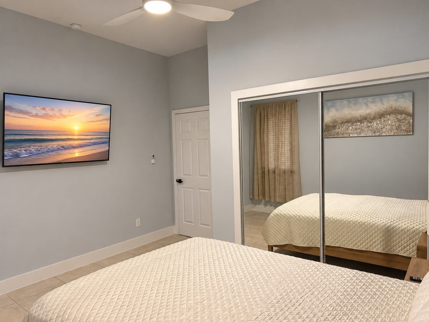A bedroom with a bed, a television displaying a sunset, and a sliding door leading to another room.