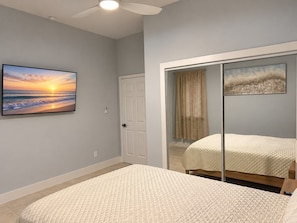 A bedroom with a bed, a television displaying a sunset, and a sliding door leading to another room.