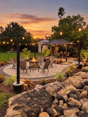 A patio area with a fire pit, outdoor furniture, and string lights.