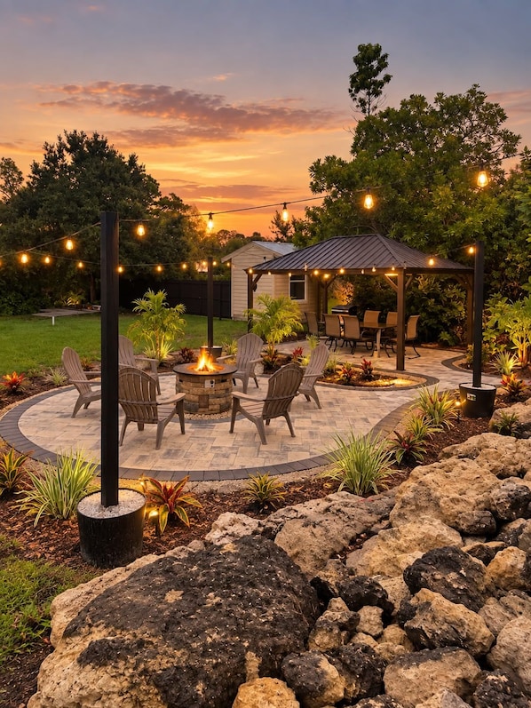 Un patio con una fogata, muebles de exterior e iluminación con luces colgantes.