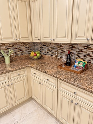 A kitchen with beige cabinets, a granite countertop, a fruit bowl, a wine bottle, and a coffee maker.